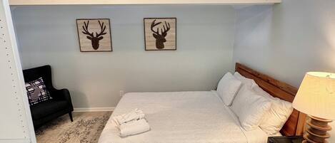 A bedroom with a bed, a nightstand, a lamp, a ceiling fan, and two deer head wall art pieces.