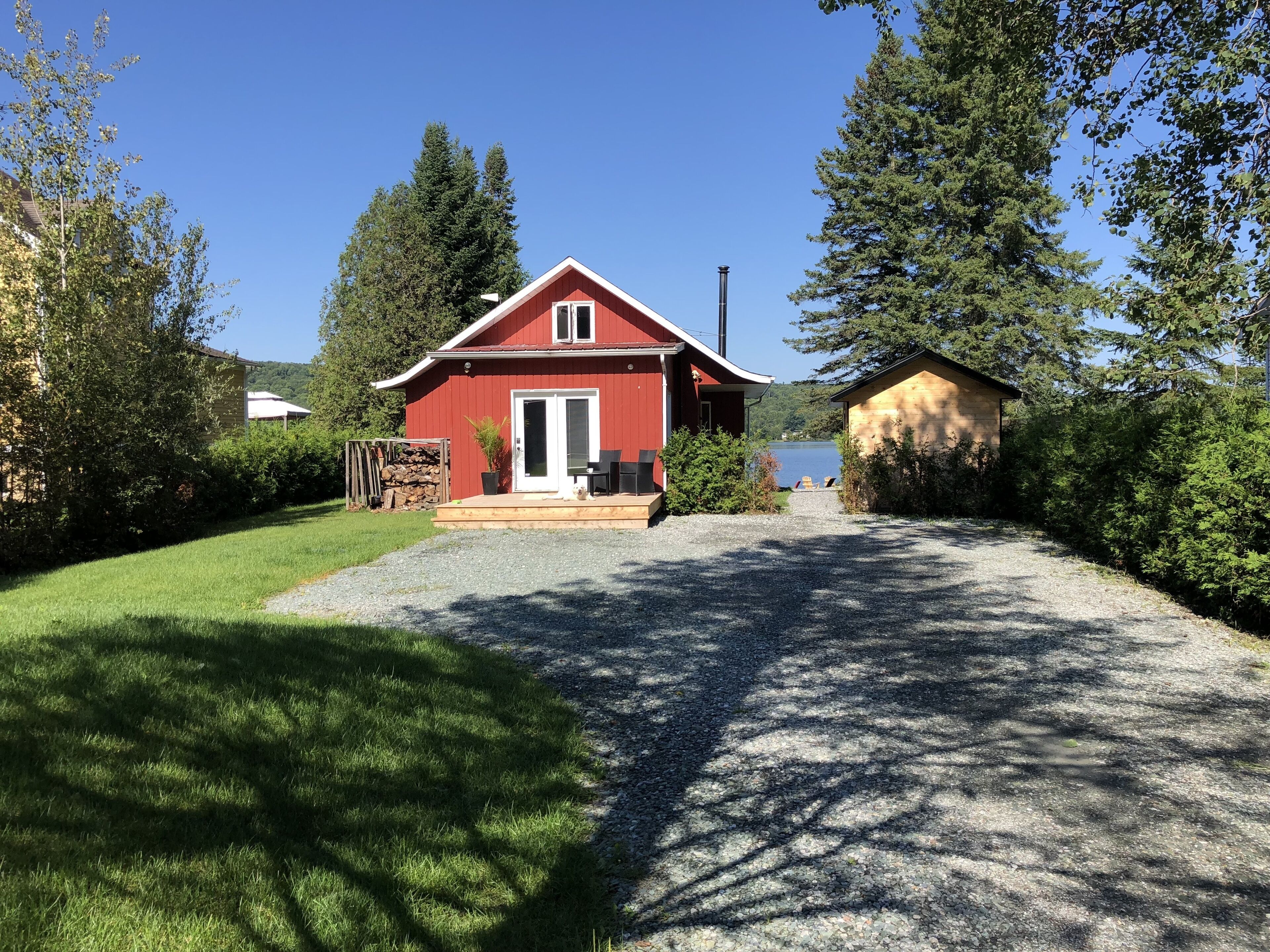 Une maison rouge avec une allée de gravier menant à une terrasse en bois aménagée avec du mobilier d’extérieur.