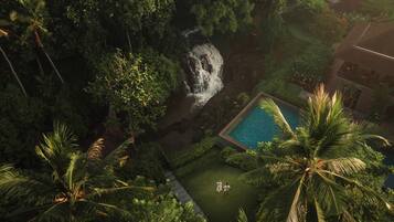 An aerial view of a lush garden with a waterfall, a swimming pool, and a pathway.