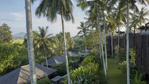 Een tropisch resort met een houten omheining, palmbomen en een pad dat leidt naar een gebouw met een schuin dak.