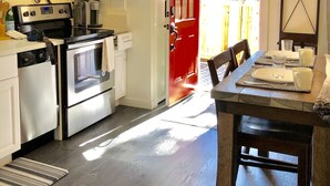 A modern kitchen with stainless steel appliances, a red door, and a dining area with a wooden table set for two.
