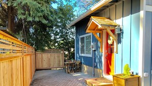 A wooden deck with a brick pattern, a wooden fence, a table with chairs, and a small wooden planter with a plant.