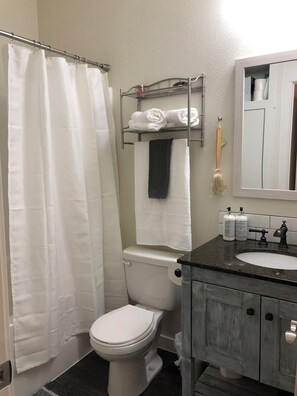 A bathroom with a white toilet, a shower curtain, a towel rack with towels, a mirror, and toiletries on the sink. - Private & Comfortable Guesthouse close to Portland +AC! (Vancouver)