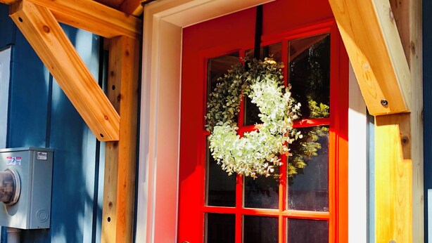 A red door with a wreath, wooden beams, and a window with a view.