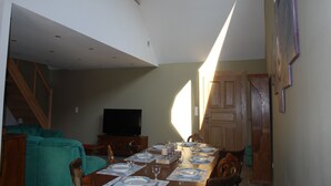 Un comedor con una larga mesa dispuesta para una comida, un televisor al fondo y una escalera que sube a un nivel superior.