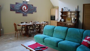 Un área de comedor con una mesa y sillas, un sofá color turquesa y un cuadro en la pared.