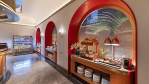 A hotel corridor with a food service area featuring a buffet with various dishes, a refrigerated beverage display, and a decorative wall with a large arched window. - Manxin Hotel Beijing Forbidden City (Beijing)