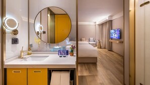 A modern hotel room with a large round mirror, dual sinks, a flat-screen TV, and a bed with a wooden floor. - Manxin Hotel Beijing Forbidden City (Beijing)