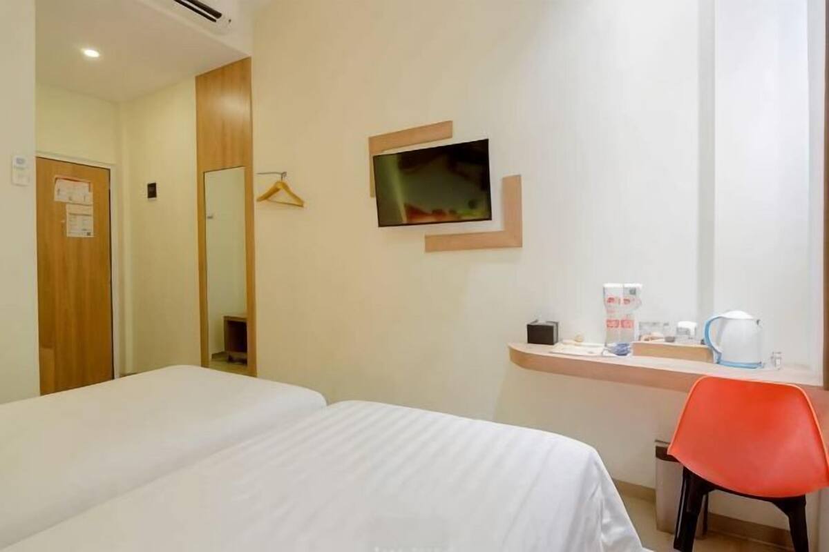 A hotel room with two beds, a TV, a desk with a coffee maker, and a mirror.
