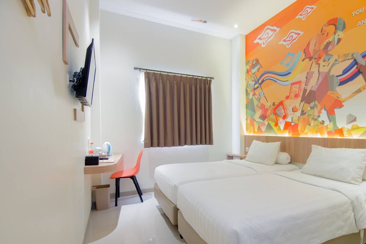 A hotel room with a large bed, a desk with a chair, a television mounted on the wall, and a colorful mural on the wall.