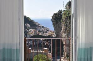 Un balcon doté d’une balustrade en fer forgé, donnant sur une ville côtière avec ses bâtiments et ses falaises.
