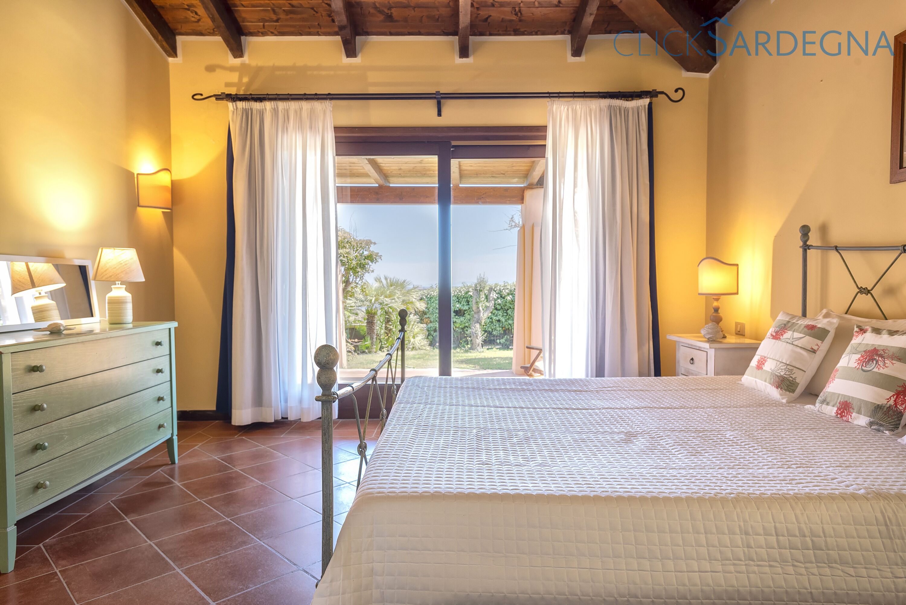 A bedroom with a bed, a dresser, a nightstand, and a view of the outdoors.