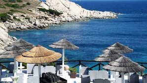 A seaside terrace with white wicker chairs, thatched umbrellas, and a rocky coastline. - Stintino Villa Regina with independent swimming pool, 3 bedrooms, 2 bathrooms (Stintino)