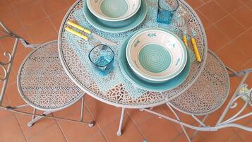 A round metal table with four plates and two glasses, surrounded by intricately designed chairs.