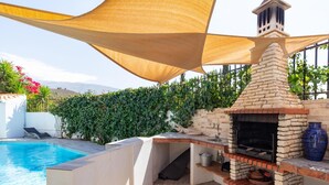 Zona junto a la piscina con una barbacoa integrada y una chimenea de piedra.