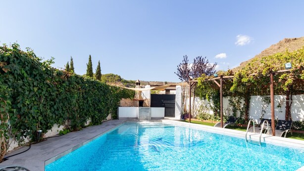 Piscina rectangular con agua azul cristalina, rodeada por un suelo de piedra y un seto verde exuberante.