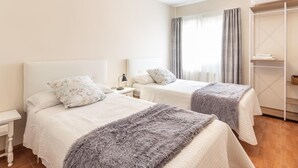 Habitación de hotel con dos camas, un armario, una mesita de noche y una lámpara colgante.