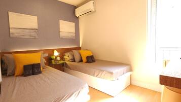 Habitación de hotel con dos camas, una mesita de noche con lámpara y un equipo de aire acondicionado en la pared.