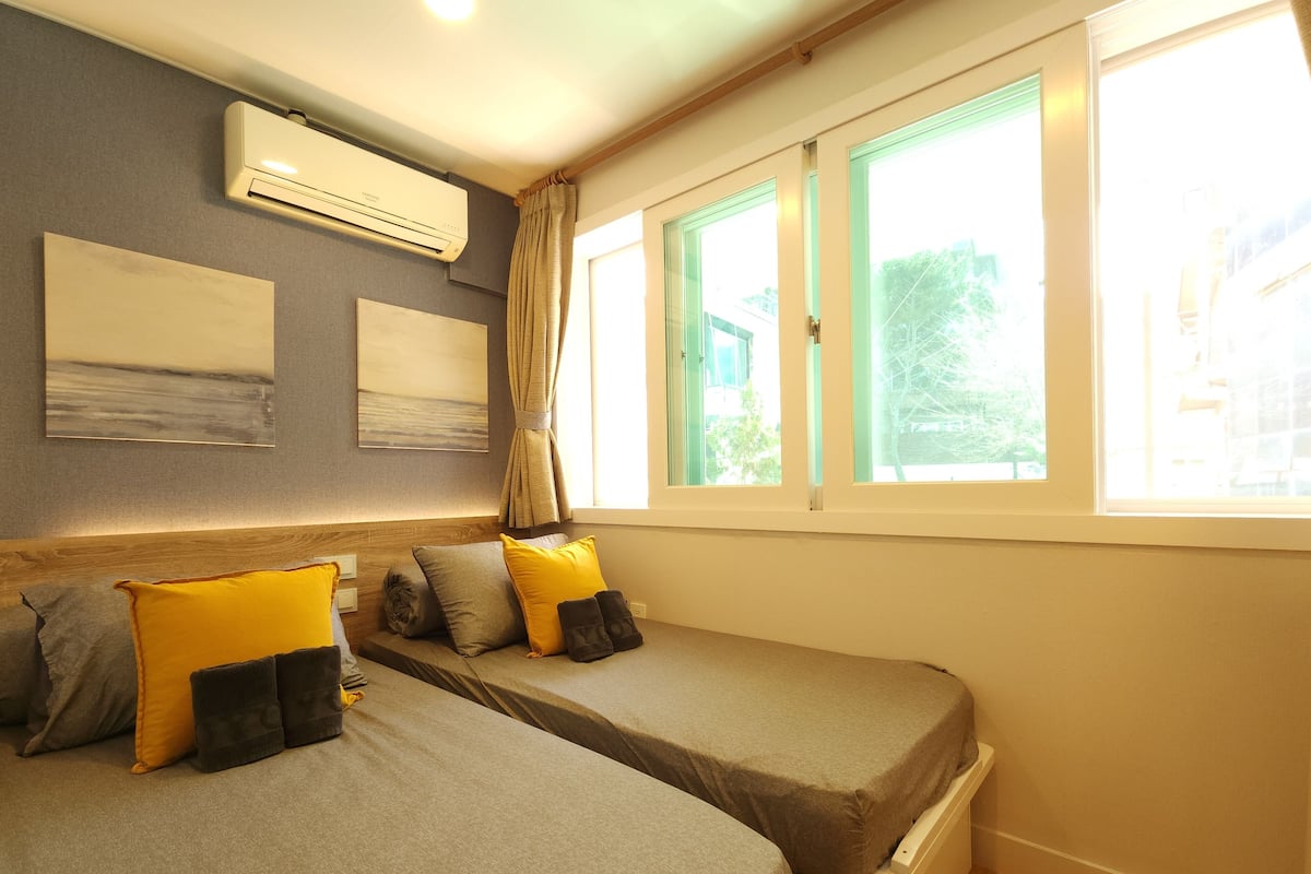 A room with two beds, a window, and an air conditioning unit.
