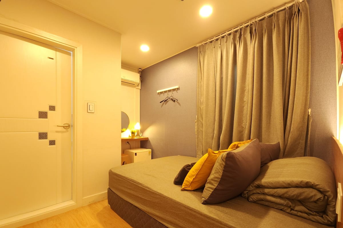 A bedroom with a bed, a bedside table with a lamp, a wall-mounted air conditioner, and a door.