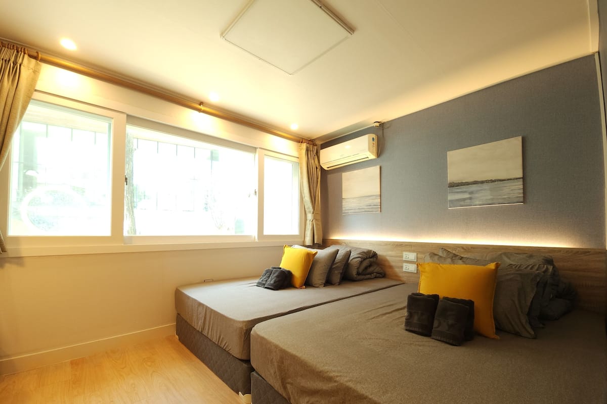 A bedroom with two beds, a window, an air conditioner, and a painting on the wall.
