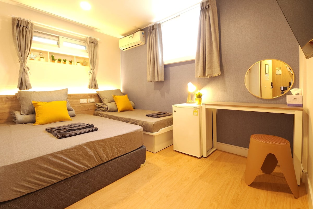 A hotel room with two beds, a desk, a small refrigerator, and a mirror.