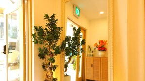 A hallway with a large mirror, a potted plant, and a cabinet with flowers. - OYO Myeongdong 5 Lodge (Seoul)