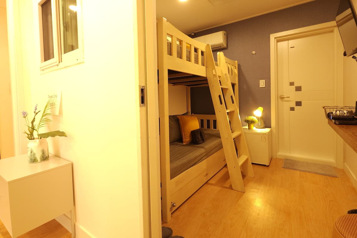 A compact room with bunk beds, a small bedside table with a lamp, and a door with a mat.