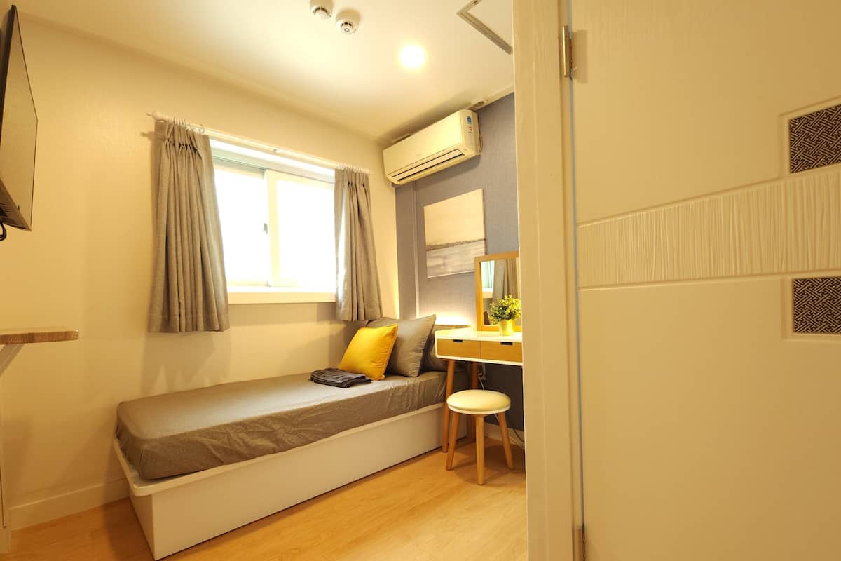 A compact bedroom with a single bed, a desk, and a chair.