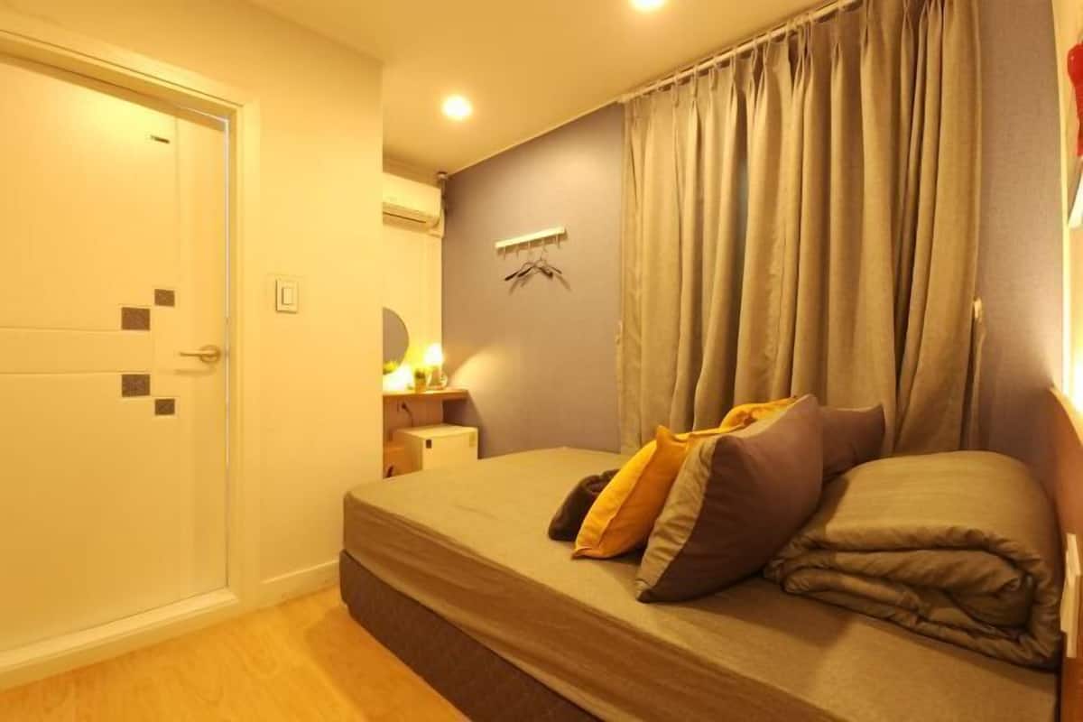 A bedroom with a bed, curtains, a bedside table, and a wall-mounted air conditioning unit.