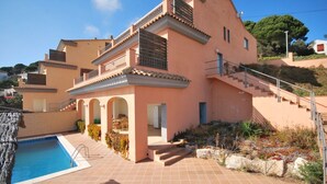 A two-story house with a swimming pool, outdoor seating, and a staircase leading to a balcony.