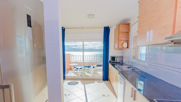 A modern kitchen with a view to a balcony, a refrigerator, and a dining area with chairs.