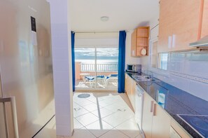 Une cuisine moderne donnant sur un balcon, équipée d’un réfrigérateur et comprenant un coin repas avec des chaises.