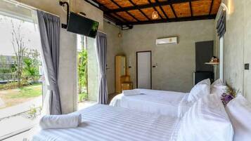A hotel room with two beds, a TV, a window with curtains, and a view of greenery outside.