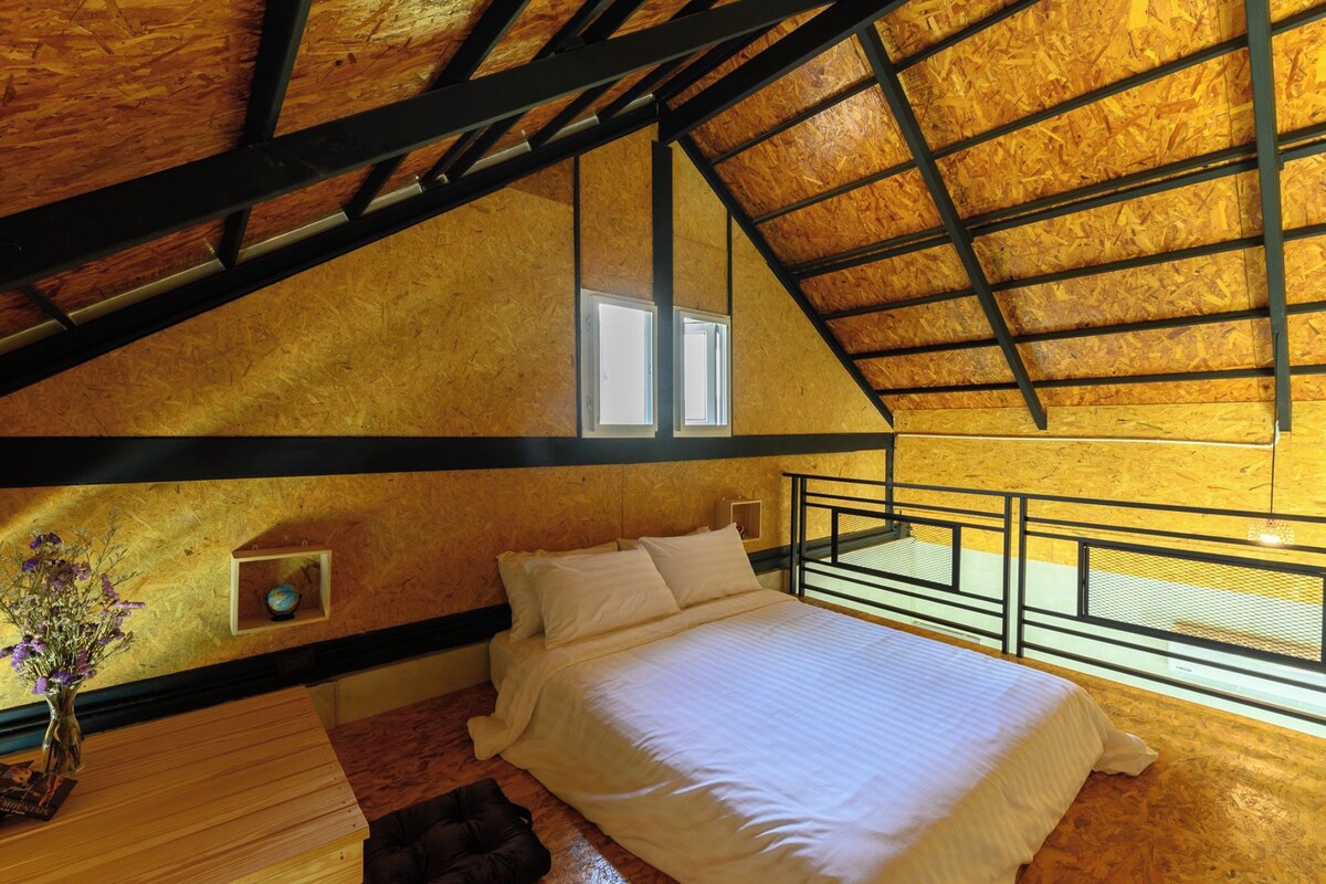 A bedroom with a sloped ceiling, a bed, a window, and a small shelf with a globe.