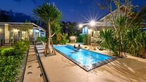 A swimming pool with a tiled deck, surrounded by palm trees and a building with a modern design. - Loftpical Resort (Ko Kaeo)