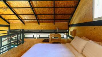 A bedroom with a wooden ceiling, a bed, a small table, and a window.