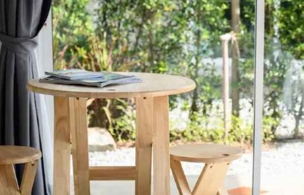 A round wooden table with a magazine on it, positioned near a window with a view of greenery outside. - Loftpical Resort (Ko Kaeo)