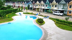 Une piscine entourée de chaises longues, elle-même bordée d’un jardin aménagé et d’une rangée de maisons de ville aux couleurs vives.