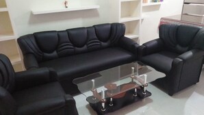 Un ensemble de canapés en cuir noir, accompagné d’une table basse en verre, dans un salon moderne.