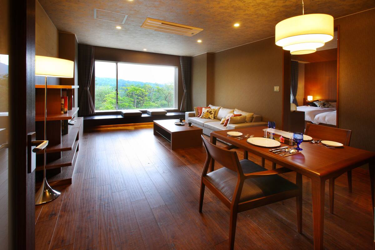 Ein modernes Hotelzimmer mit Essbereich, einer Couch und einem großen Fenster mit Blick ins Freie.