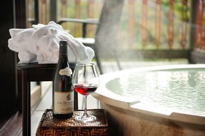 A bottle of Les Meyssonier Crozes 2000 wine and a glass of red wine on a woven coaster, placed on a table next to a hot tub. - Fontaine Bleau Sengokutei (Hakone)