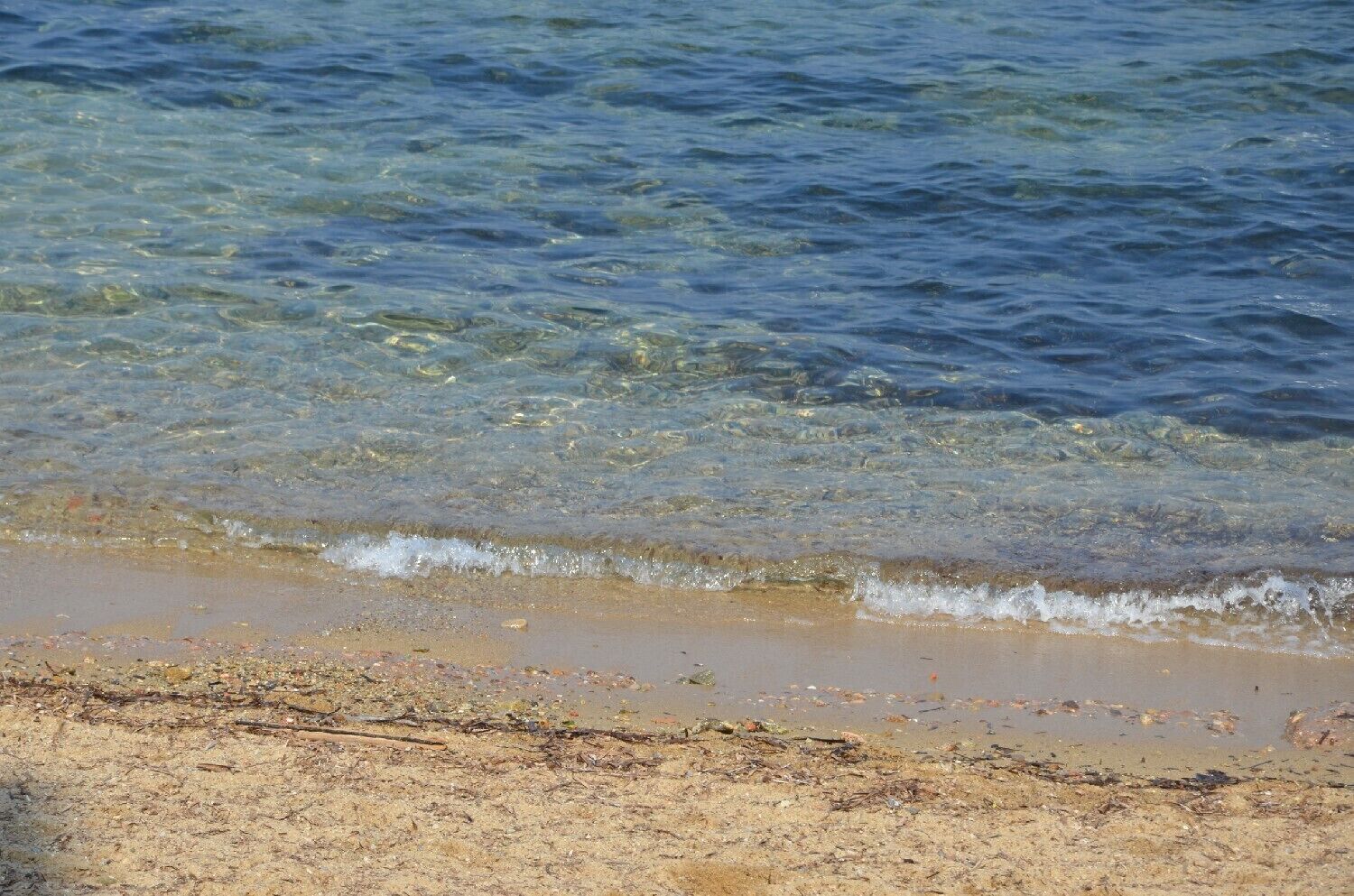 Een strand met helder water, zandstrand en wat vuil.