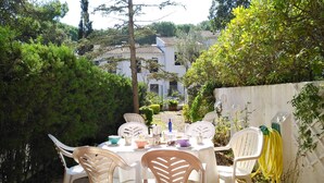 An outdoor patio with a round table and white plastic chairs, surrounded by greenery and a white fence. - 1PX 65 - Cozy house for 8 people with communal pool only 800m from the Calella de Palafrugell beach (Calella de Palafrugell)