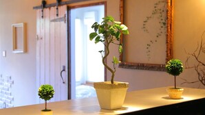 A room with a wooden floor, a large window, and a door. There are three potted plants on a table. - Fujinokura Tiny Fort (Fujiyoshida)
