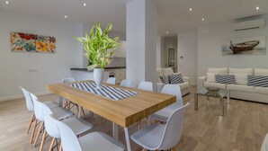 Un salon moderne avec une table à manger en bois, des chaises blanches, une table basse en verre et un canapé blanc agrémenté de coussins à motifs.