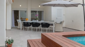 Une terrasse extérieure avec une table à manger, des chaises et un espace piscine.