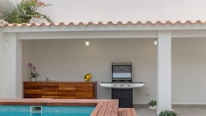 Un espace aménagé au bord de la piscine, avec une terrasse en bois, un barbecue et une petite plante en pot.