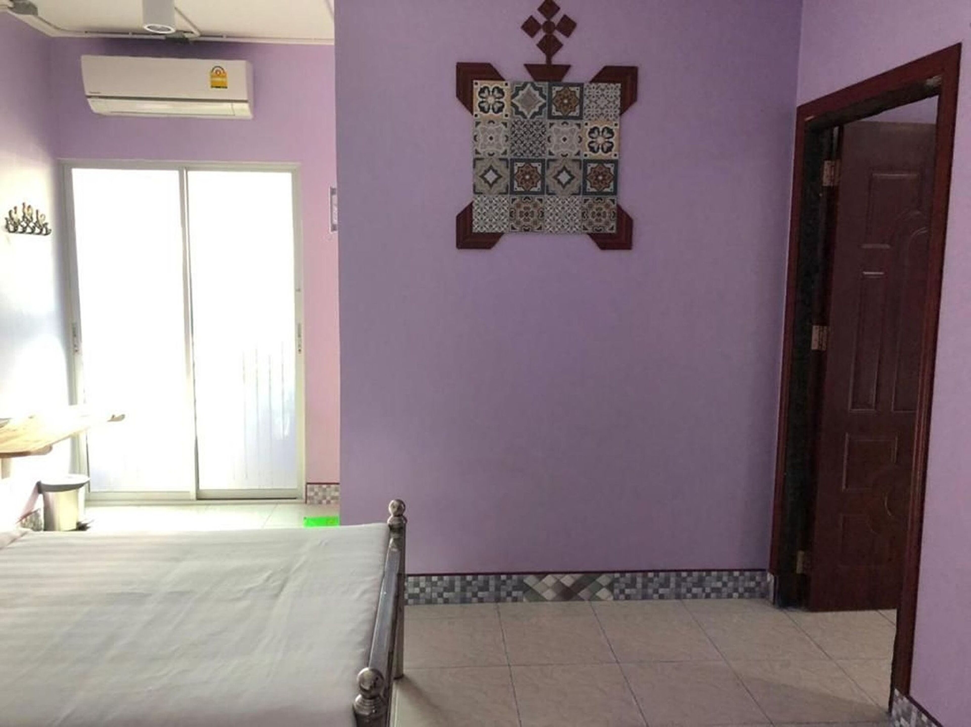 Una habitación con una cama, un azulejo decorativo en la pared, una puerta y una ventana.