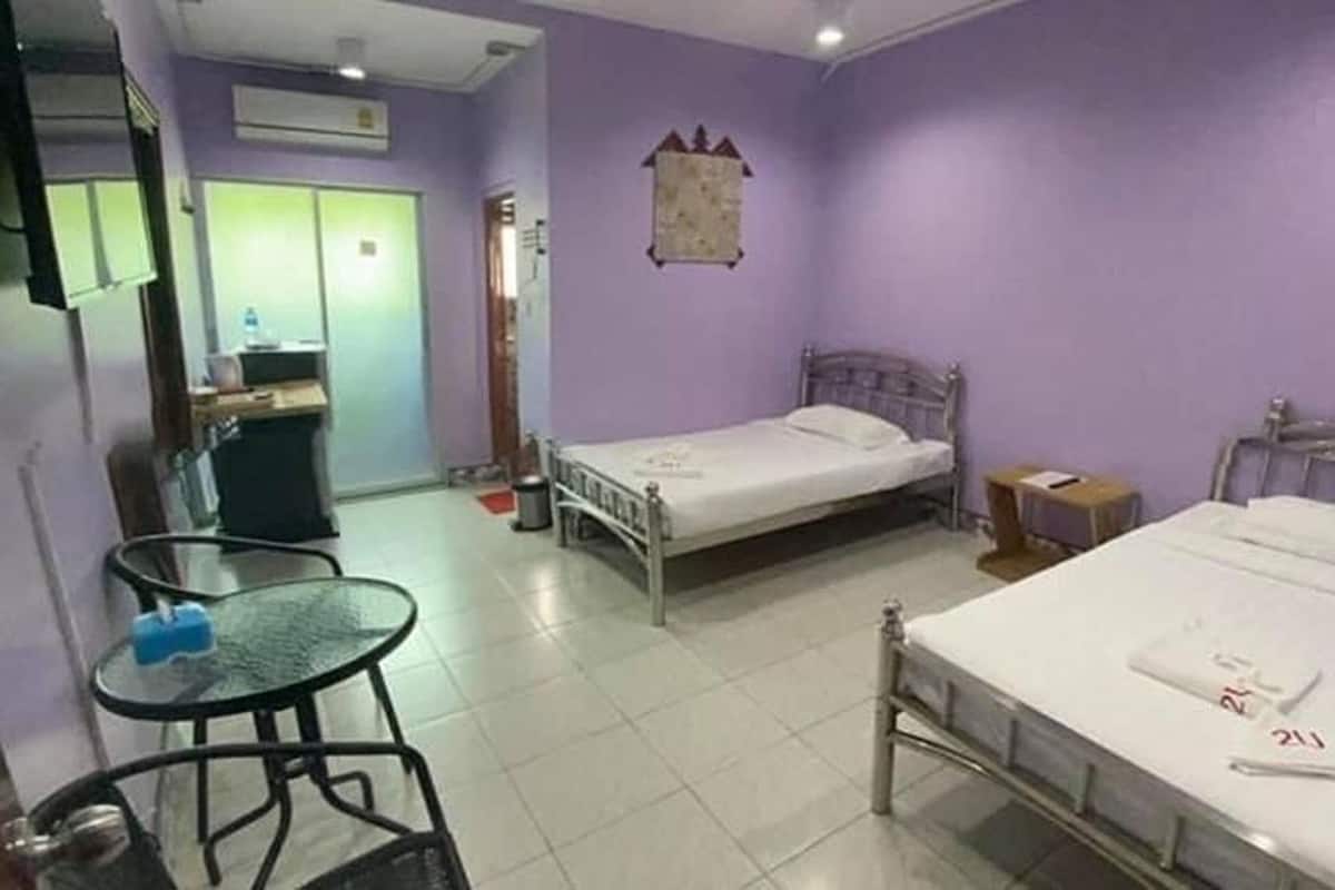 A hotel room with two single beds, a small table, a chair, a desk, and a wardrobe.
